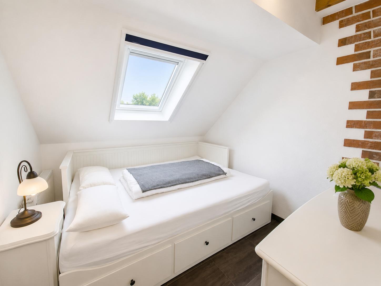 Schlafzimmer mit Dachfenster, weißem Bett und Holzwandverkleidung.
