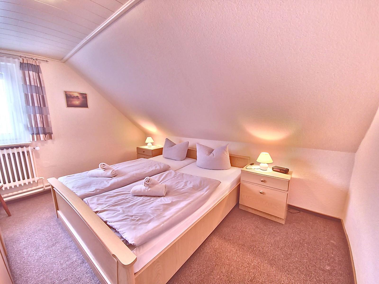 Schlafzimmer mit Doppelbett, zwei Nachttischen und Fenster mit Vorhängen.
