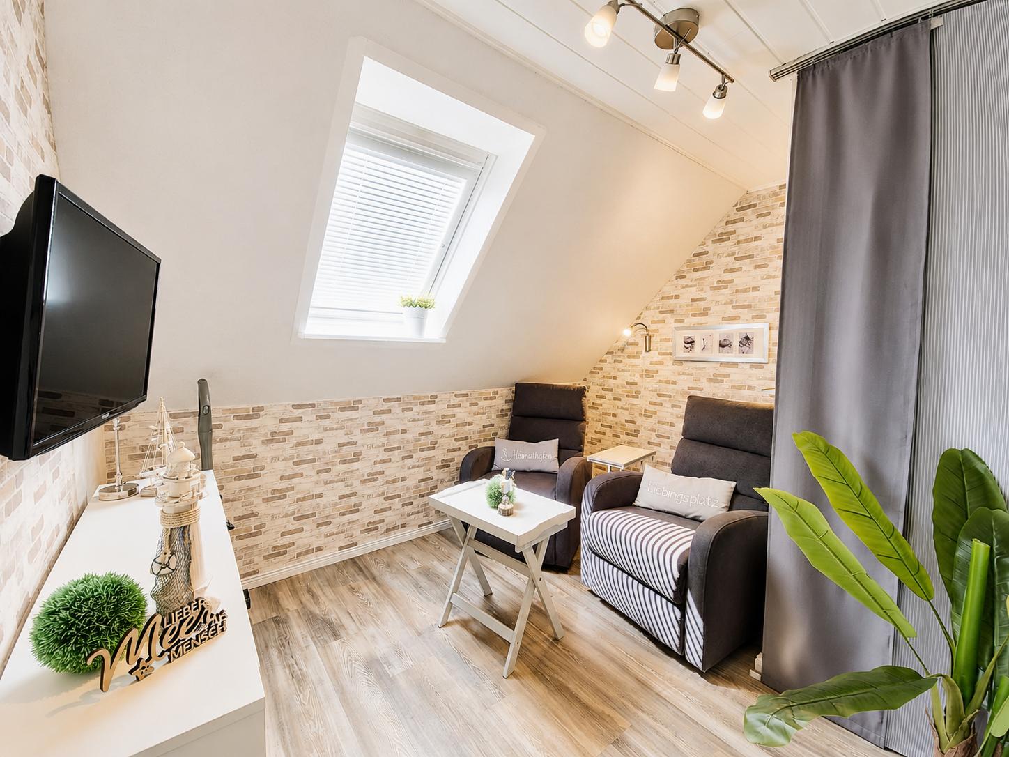 Dachgeschosszimmer mit TV, Sitzgelegenheiten und Dachfenster.
