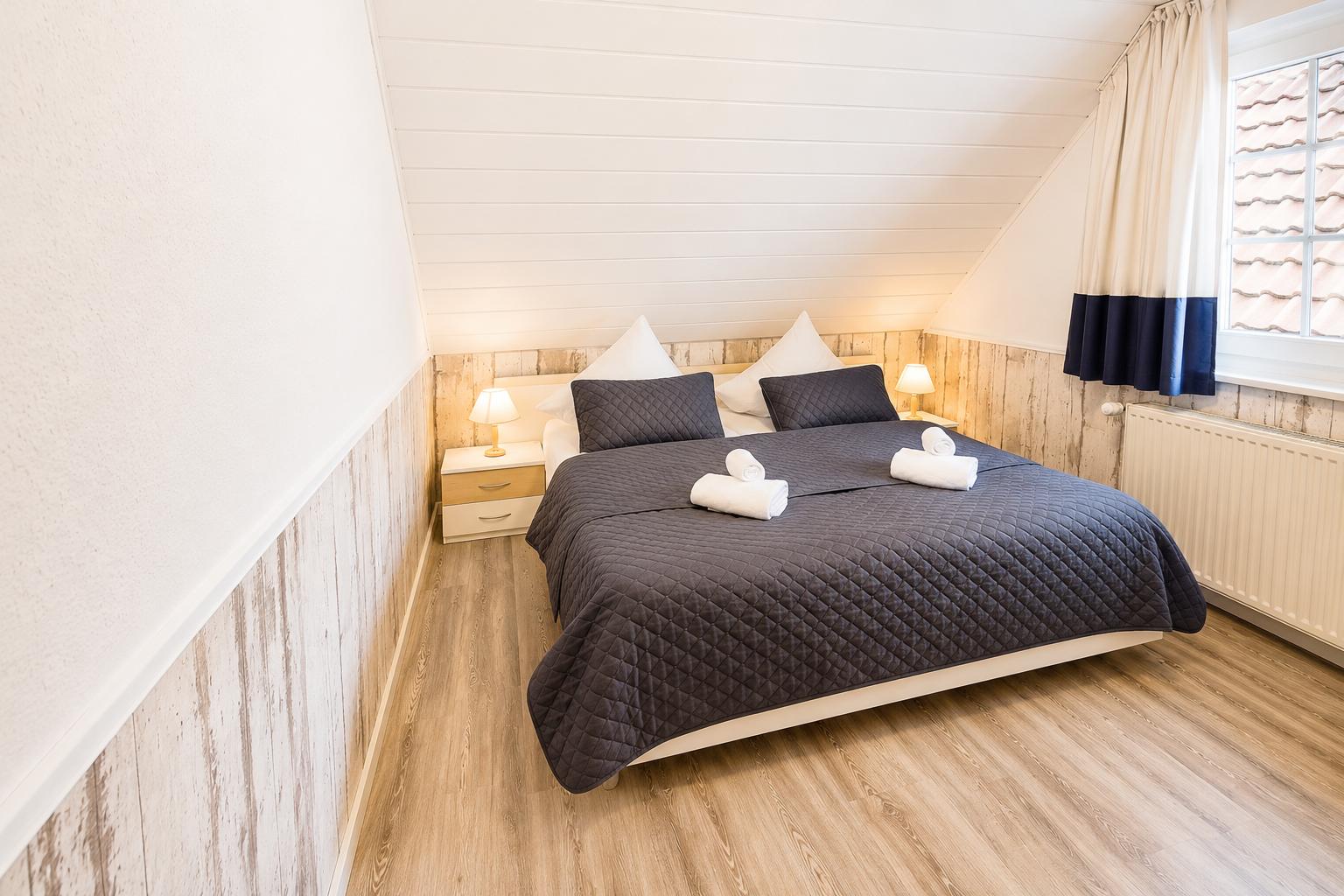 Schlafzimmer mit Doppelbett, Holzwand und Fenster mit Blick auf Dachziegel.