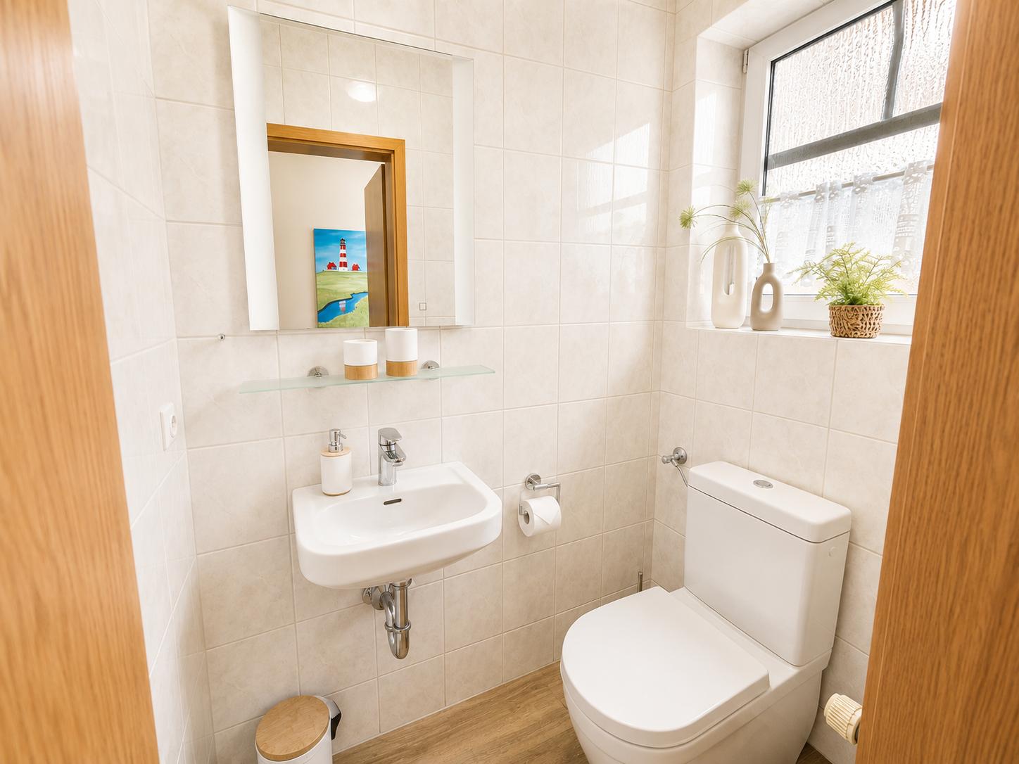 Badezimmer mit Toilette, Waschbecken und Spiegel. Fenster mit Pflanzen.