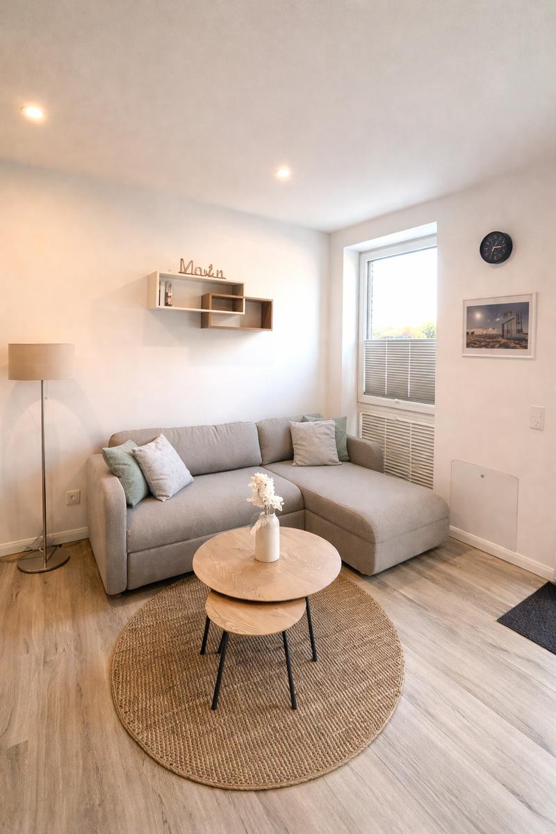 Ein Wohnzimmer mit grauem Sofa, runden Tischen und Holzboden.