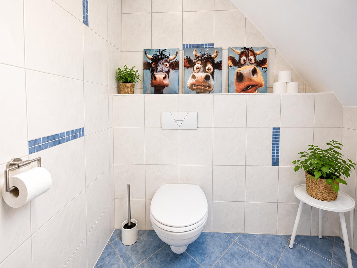 Badezimmer mit Toilette, drei Kuh-Bildern und Pflanzen.