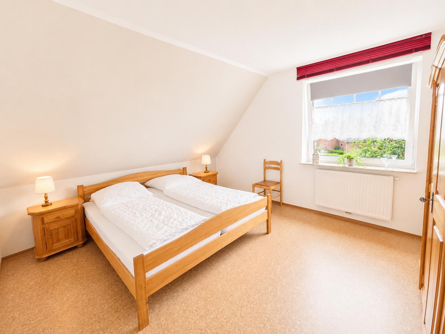 Schlafzimmer mit Doppelbett, zwei Nachttischen und Stuhl. Fenster mit Blick auf Garten.
