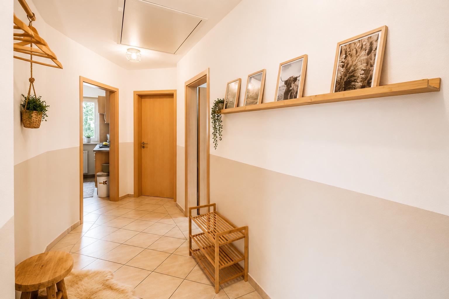 Flur mit Holzregal, Bildern und Schuhschrank. Küche und Tür im Hintergrund.