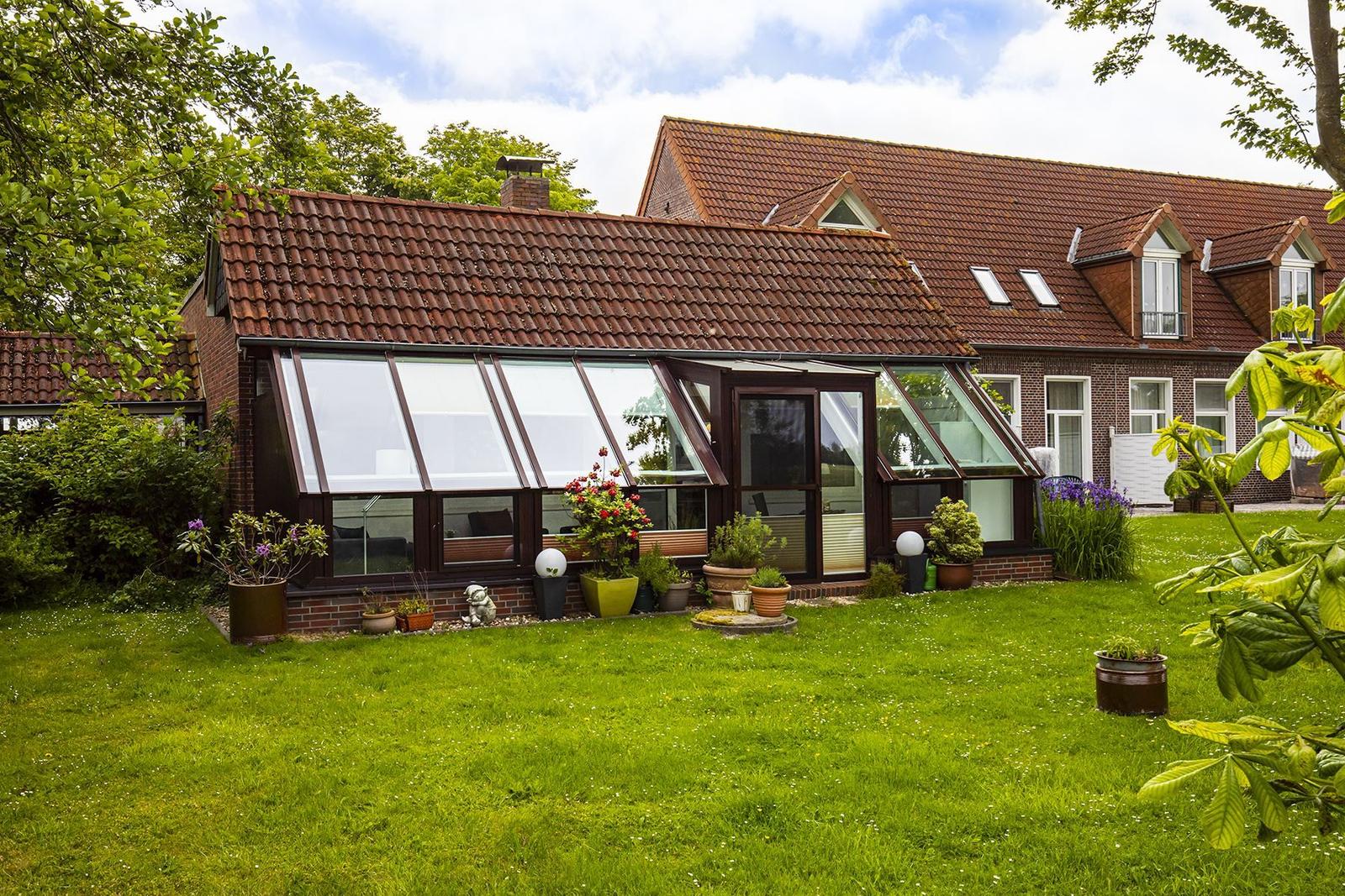 Haus mit Glasveranda und Garten. Roter Ziegeldach, Pflanzen und Rasen.