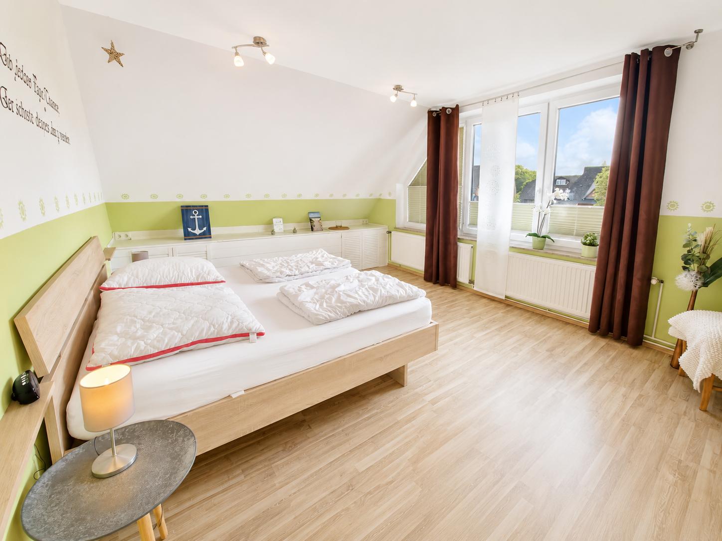 Schlafzimmer mit Doppelbett, Holzboden und großem Fenster mit Blick nach draußen.