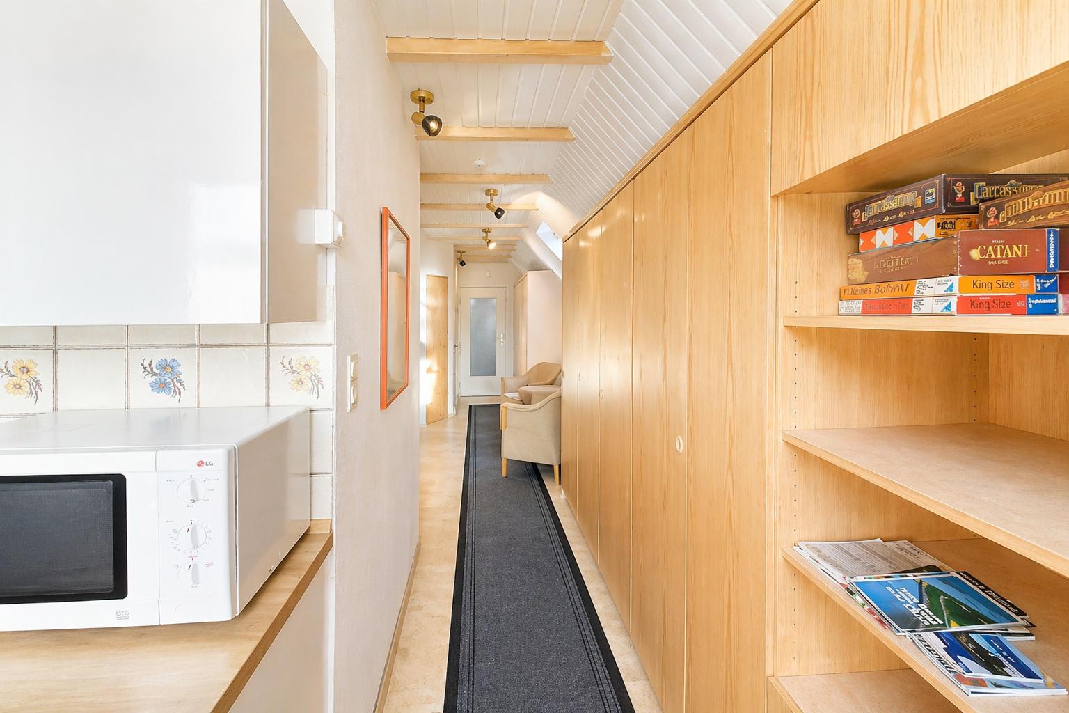 Küche mit Mikrowelle, Flur mit Holzregalen und Brettspielboxen.