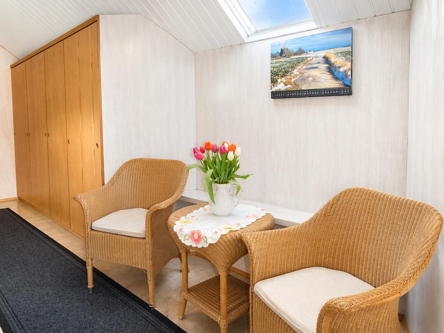 Zwei geflochtene Sessel und ein Tisch mit Blumen unter einem Dachfenster.