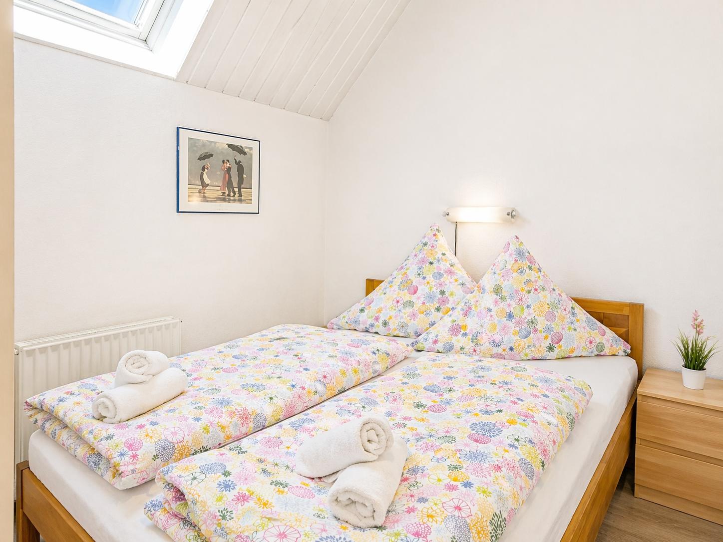 Schlafzimmer mit Doppelbett, Blumenbezug und Dachfenster.