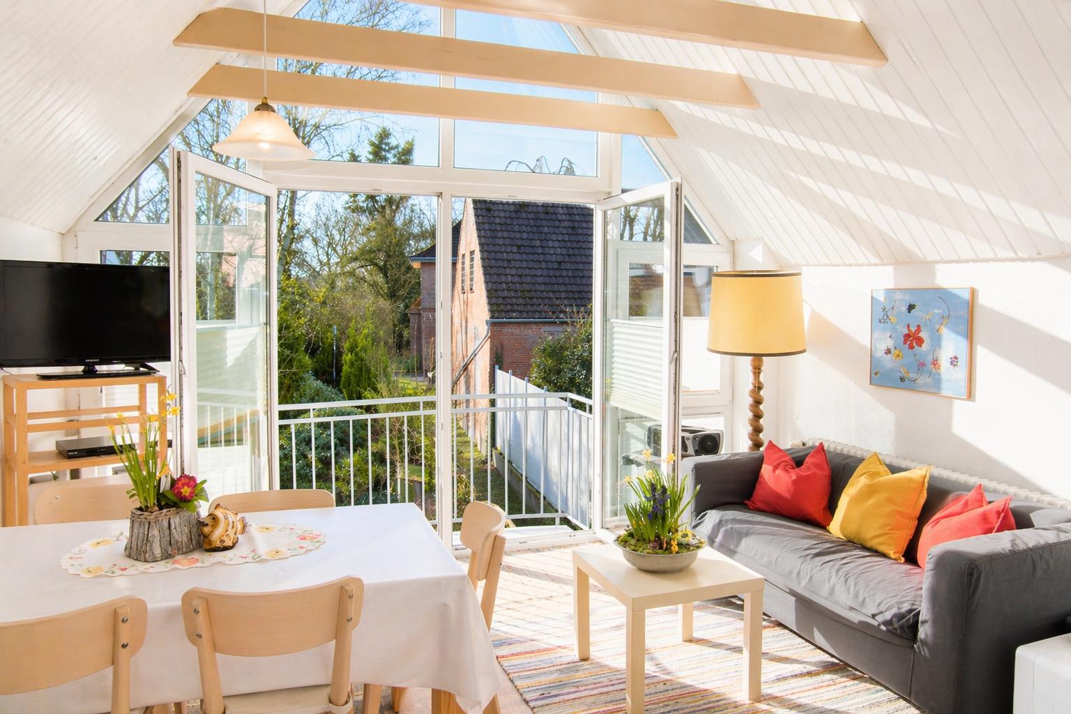 Wohn- und Essbereich mit Balkon, Sofa und Esstisch unter Holzbalken.