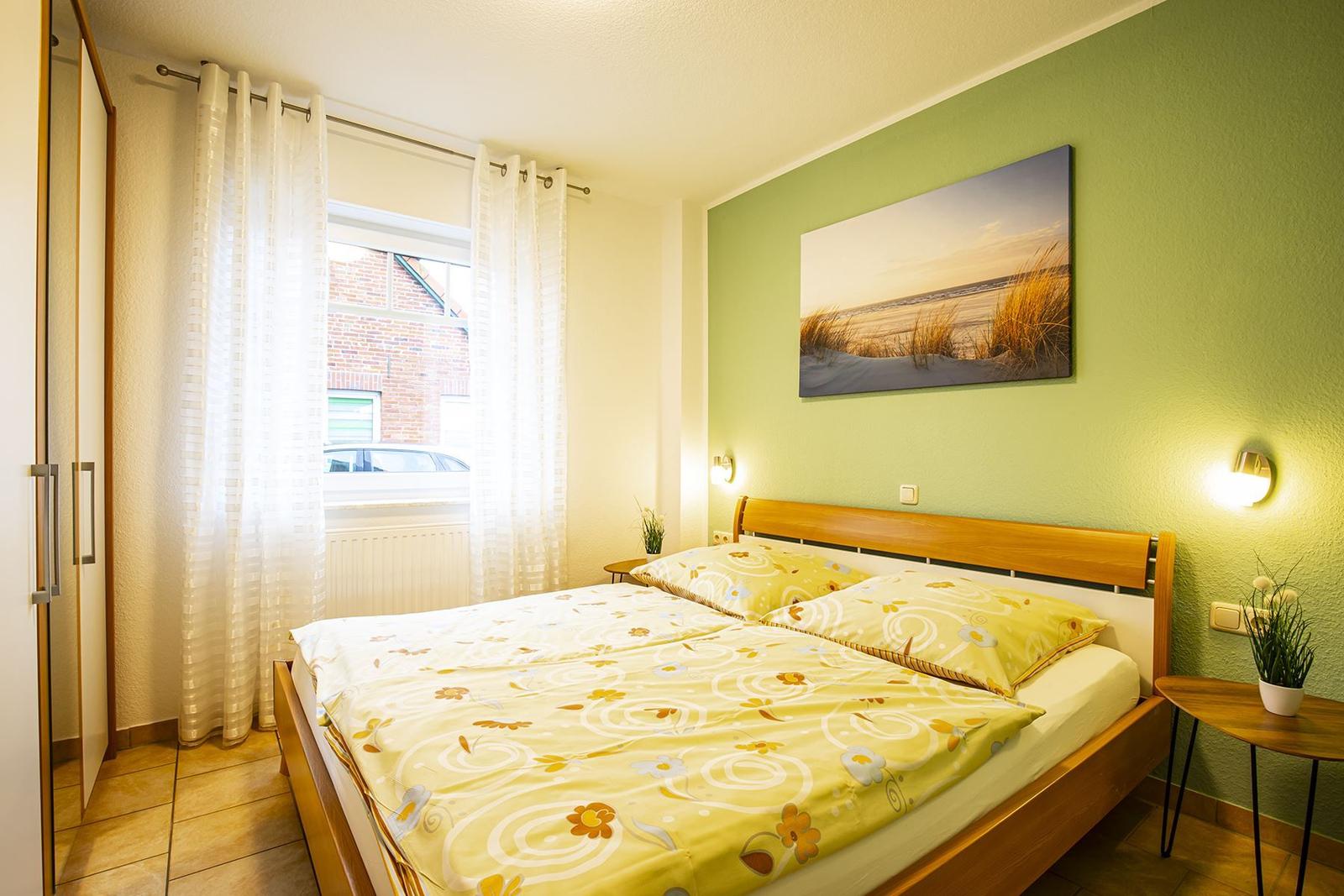 Schlafzimmer mit Doppelbett, grüner Wand und Fenster mit Vorhängen.
