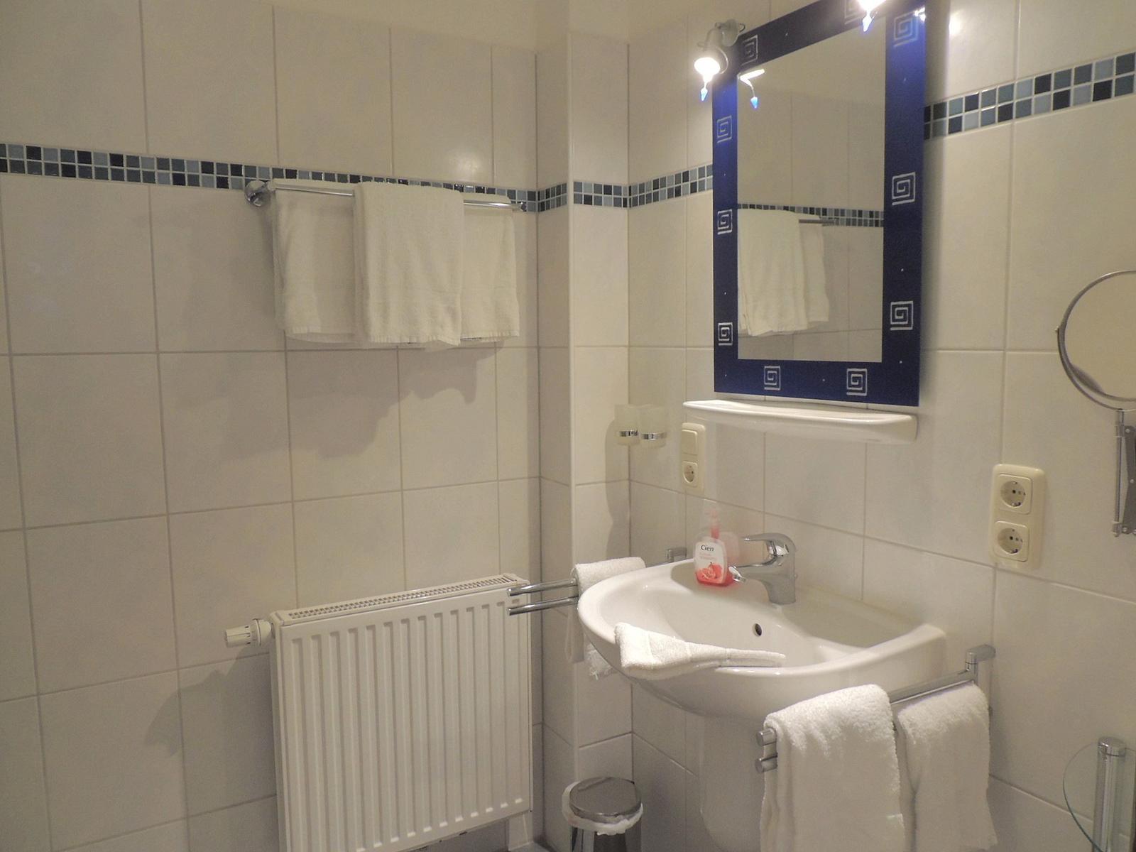 Badezimmer mit Waschbecken, Spiegel, Handtüchern und Heizkörper.