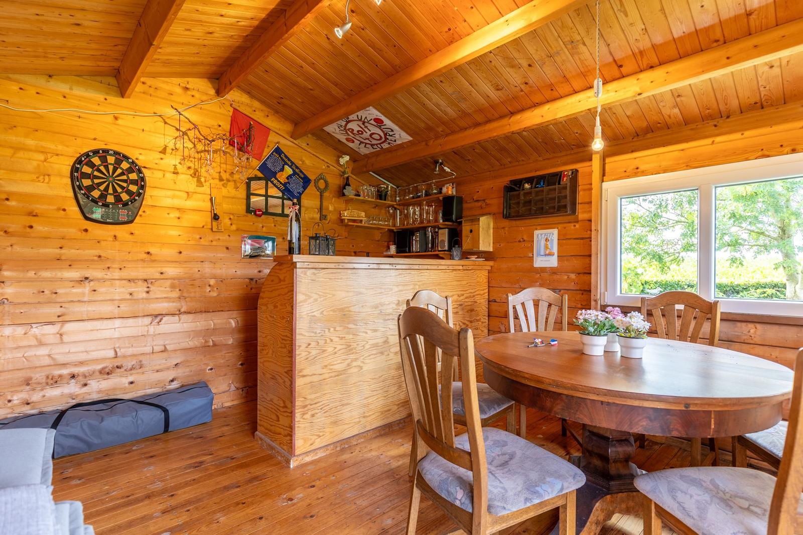 Holzvertäfelte Küche mit Essbereich, Bar und Dartboard. Fenster zeigt grüne Landschaft.