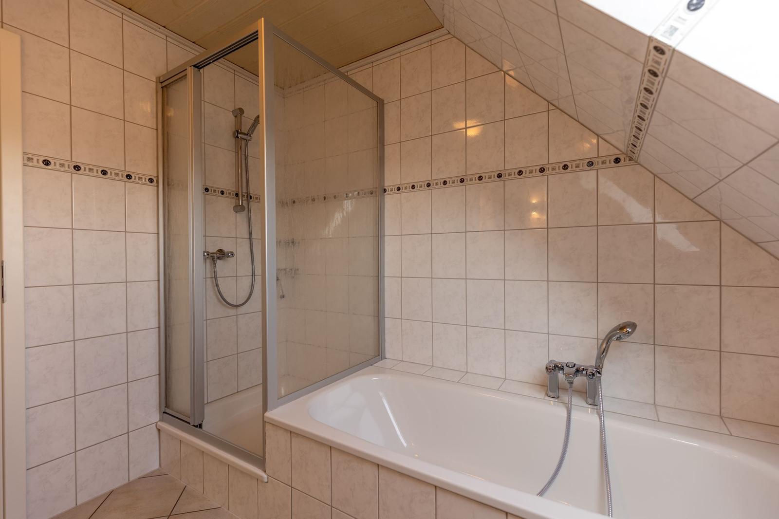 Badezimmer mit Dusche und Badewanne, belegt mit hellen Fliesen und Dachfenster.
