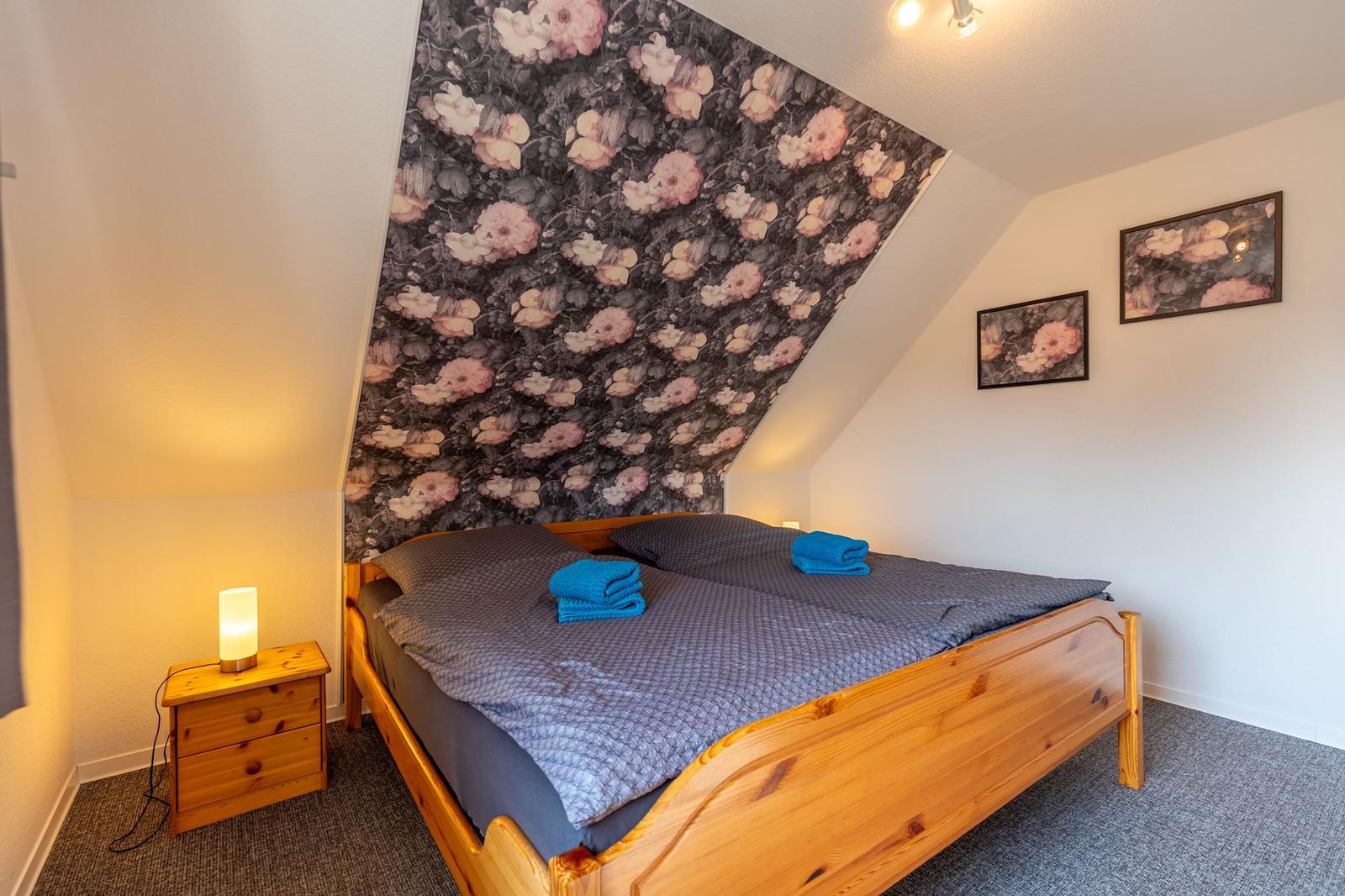 Schlafzimmer mit Holzbett, Blumenwand und Nachttisch mit Lampe.