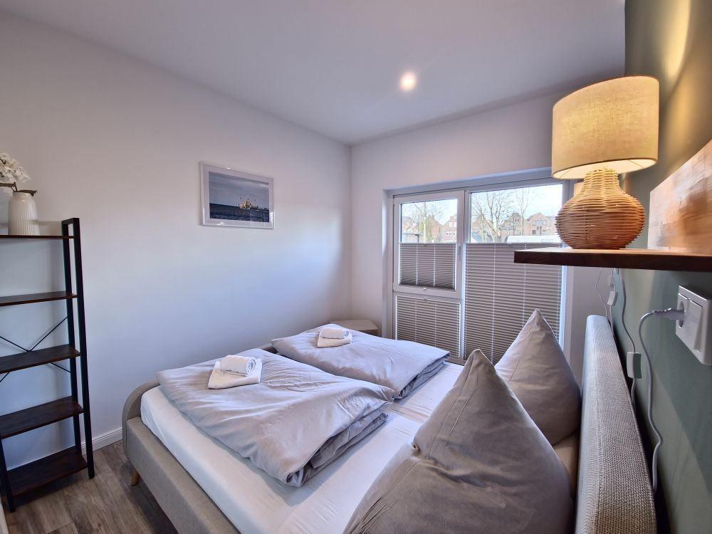 Schlafzimmer mit Bett, Nachttisch, Wandbild und Lampe. Fenster mit Jalousie.