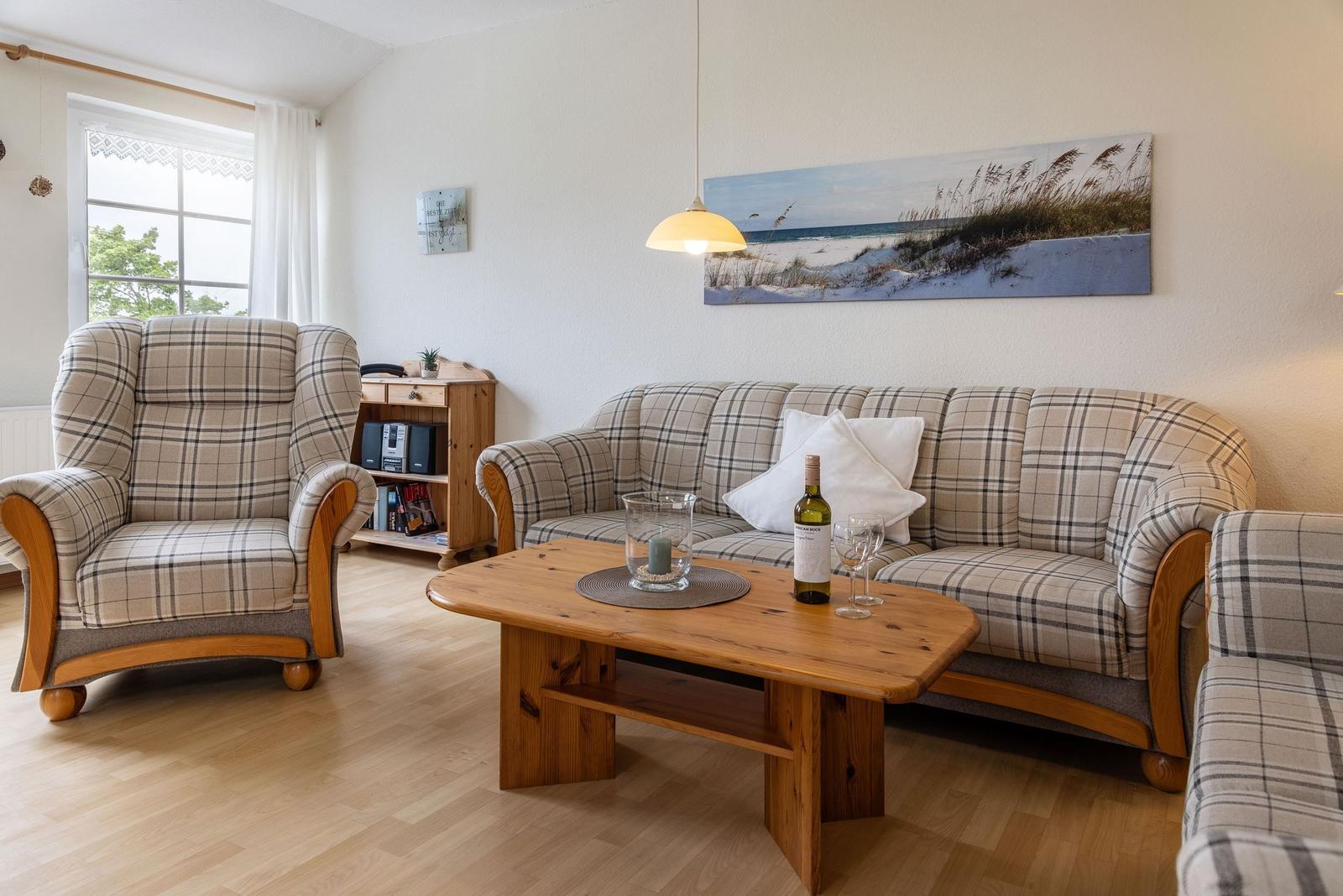 Wohnzimmer mit Sofa, Sessel und Holztisch. Wandbild zeigt Strand.