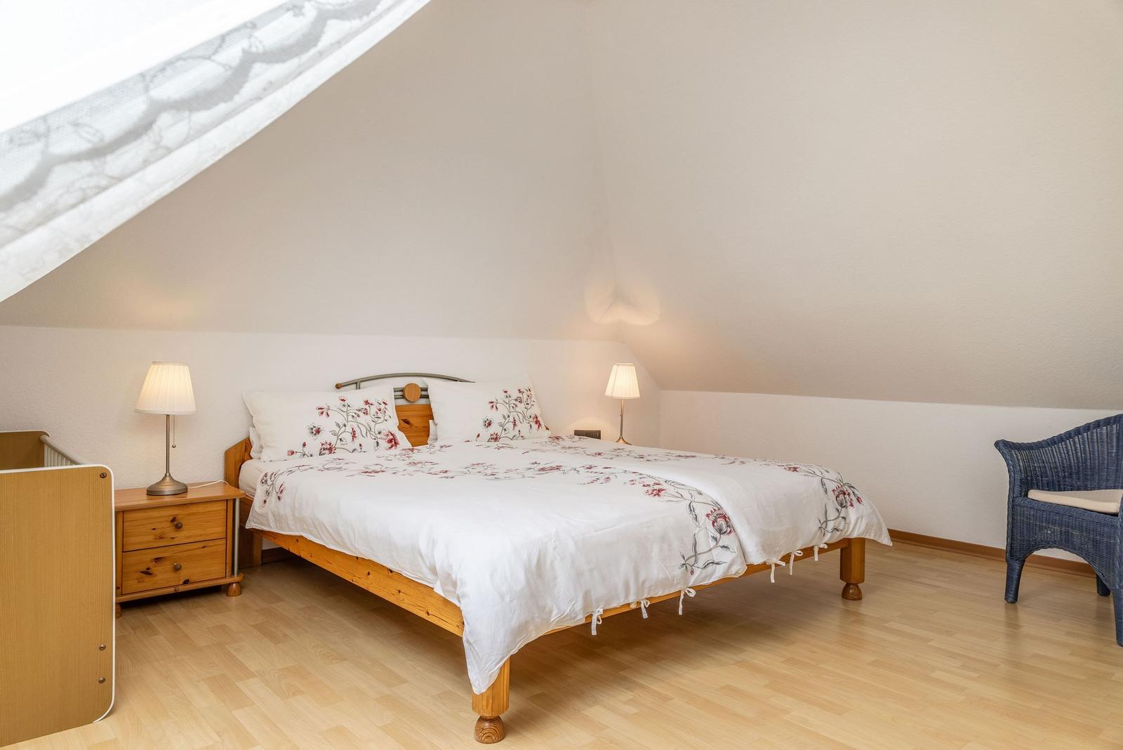 Schlafzimmer mit Dachschrägen, Bett, Nachttische und Stuhl.