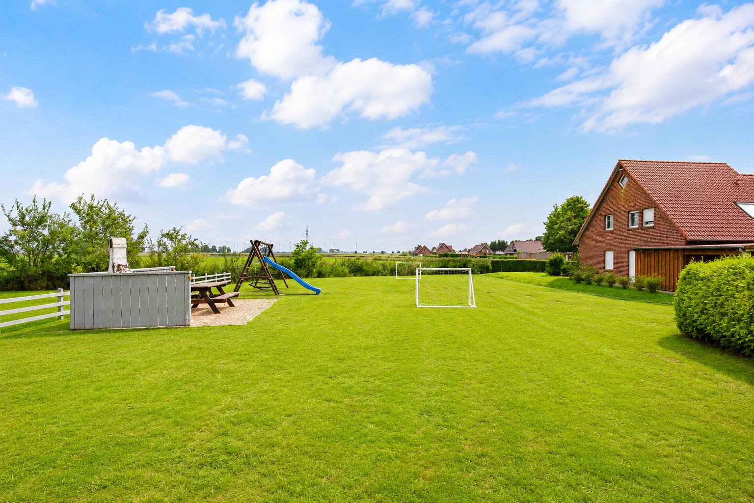 Großer grüner Garten mit Spielplatz, Grill und Fußballtor neben einem Haus.