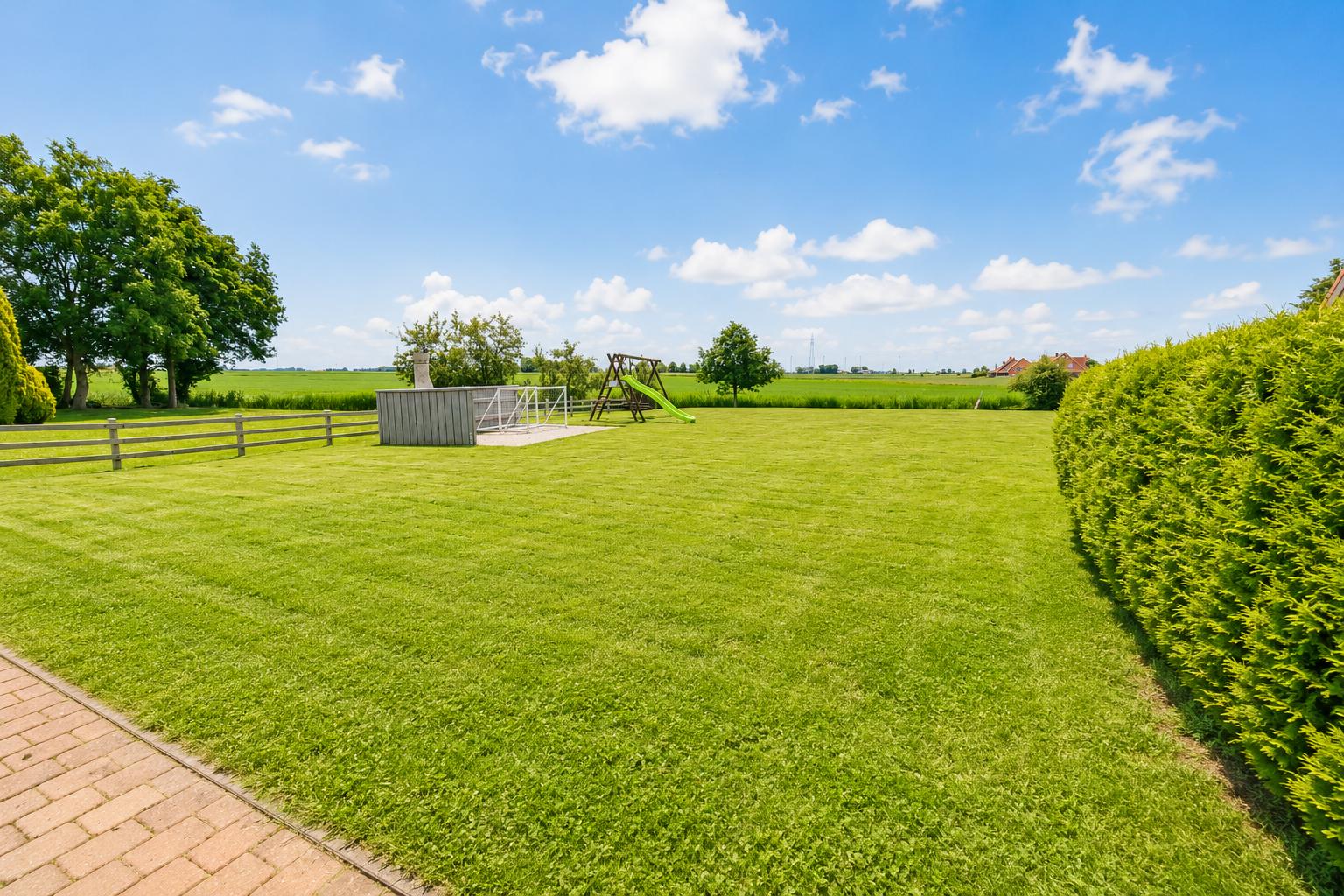 Großer grüner Garten mit Spielplatz und Grillhütte. Blick auf Felder und Himmel.