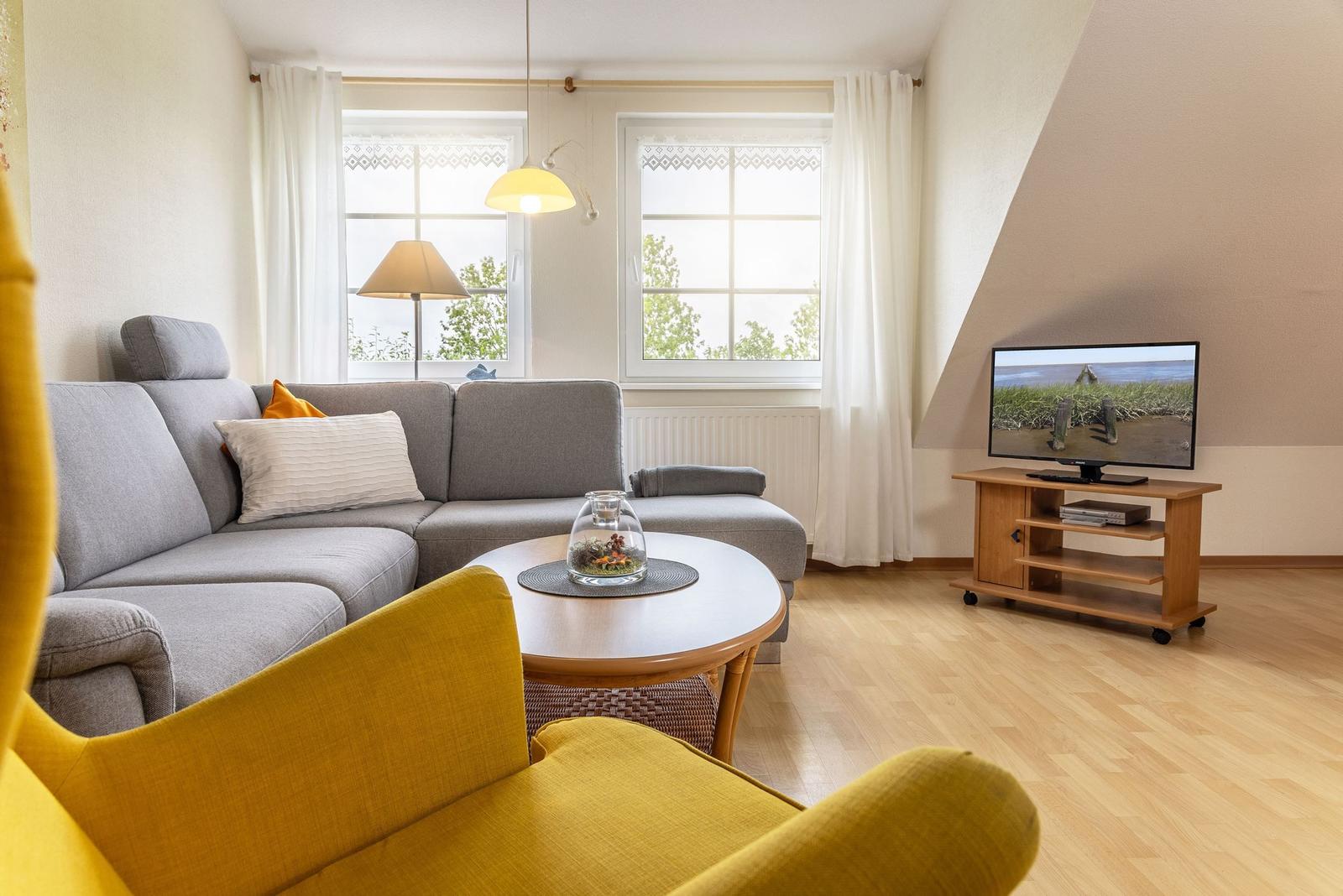 Wohnzimmer mit grauem Sofa, runden Tisch und Fernseher auf Holzstand.
