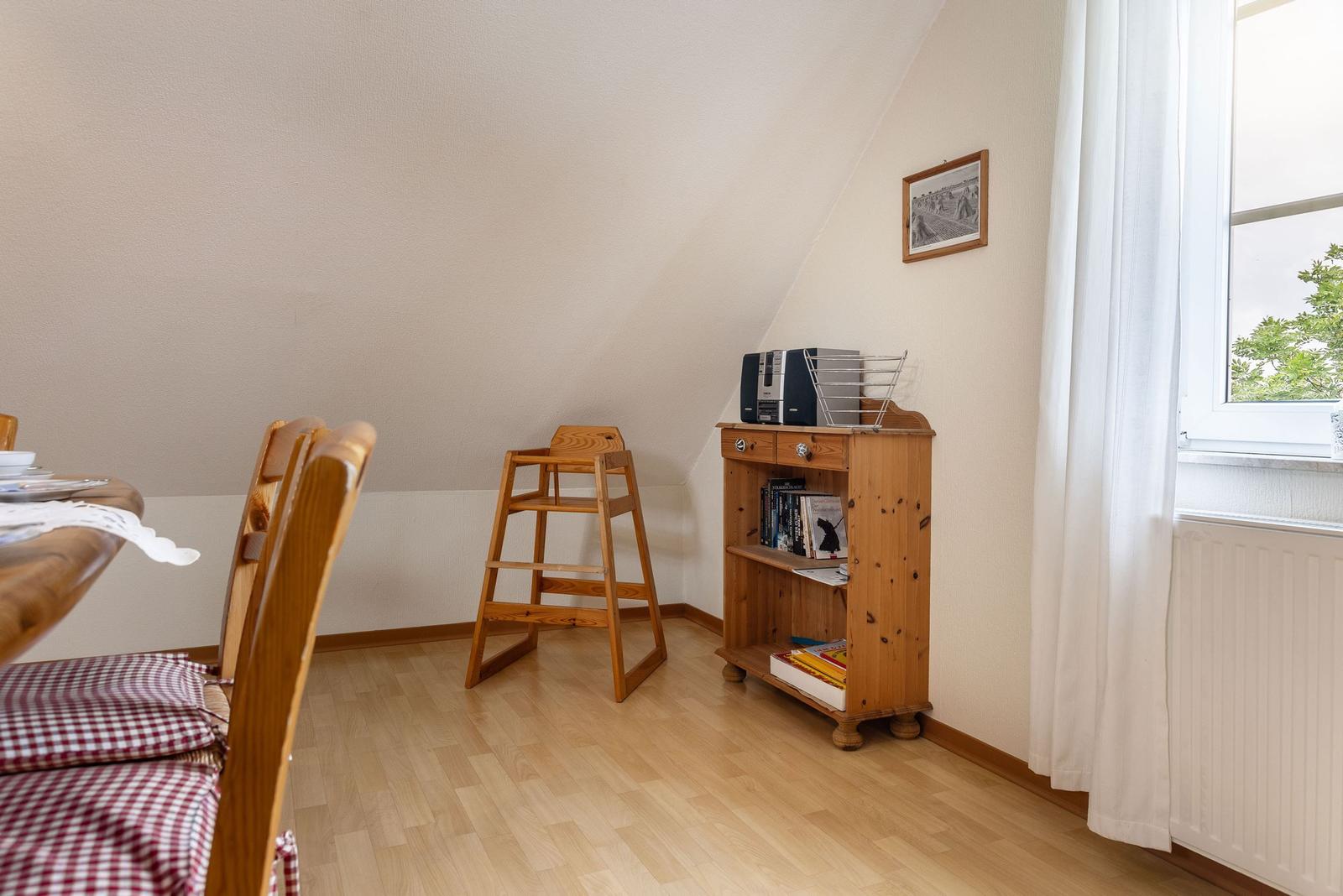 Ein Raum mit Holzmöbeln, einem Hochstuhl und einem Bücherregal unter einem Dachschrägen.