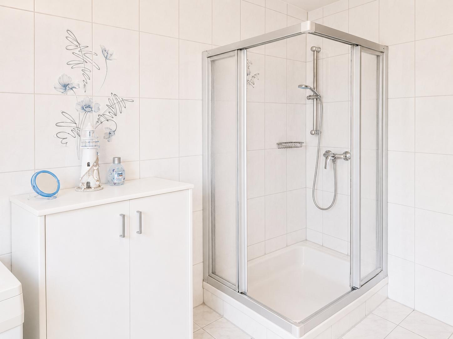Badezimmer mit Dusche, Waschbecken und Schrank. Wandfliesen und Glasduschkabine.