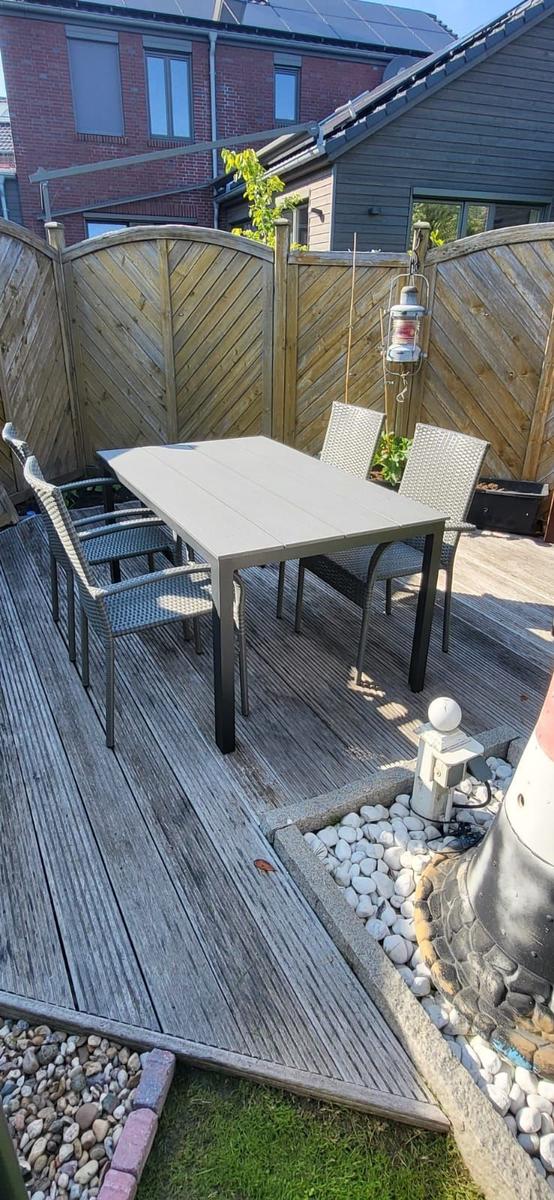 Terrasse mit Tisch und Stühlen, umgeben von Holzzaun und Steinbeeten.