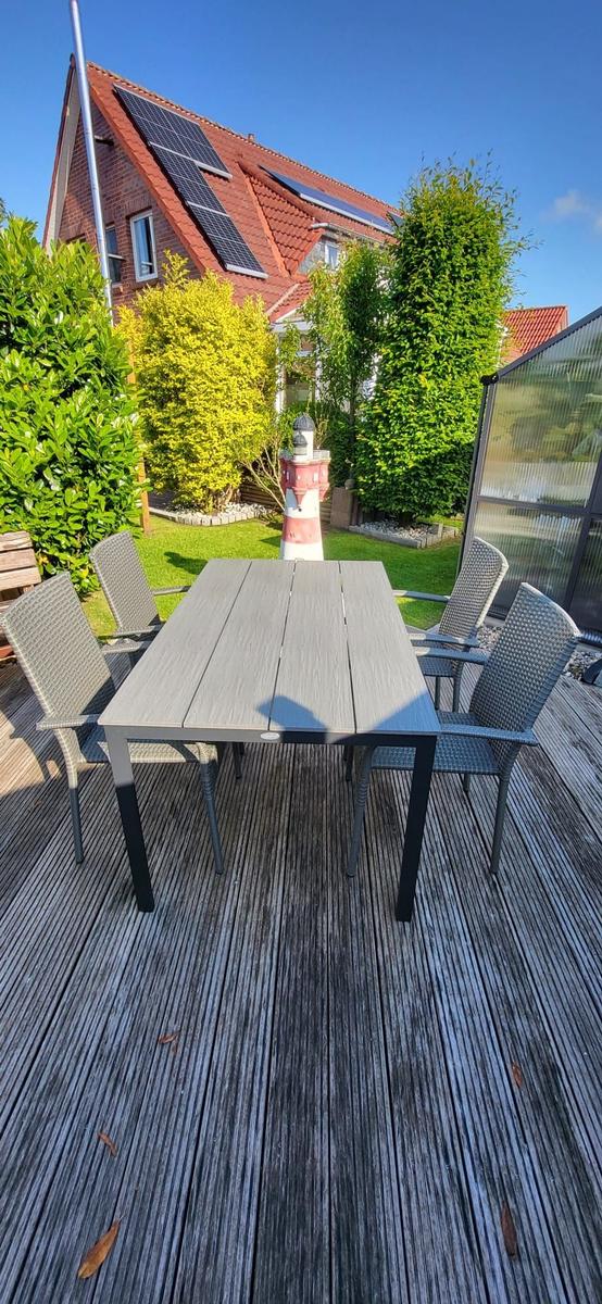 Terrasse mit Tisch und Stühlen, Blick auf Haus mit Solarpanelen und grünen Bäumen.