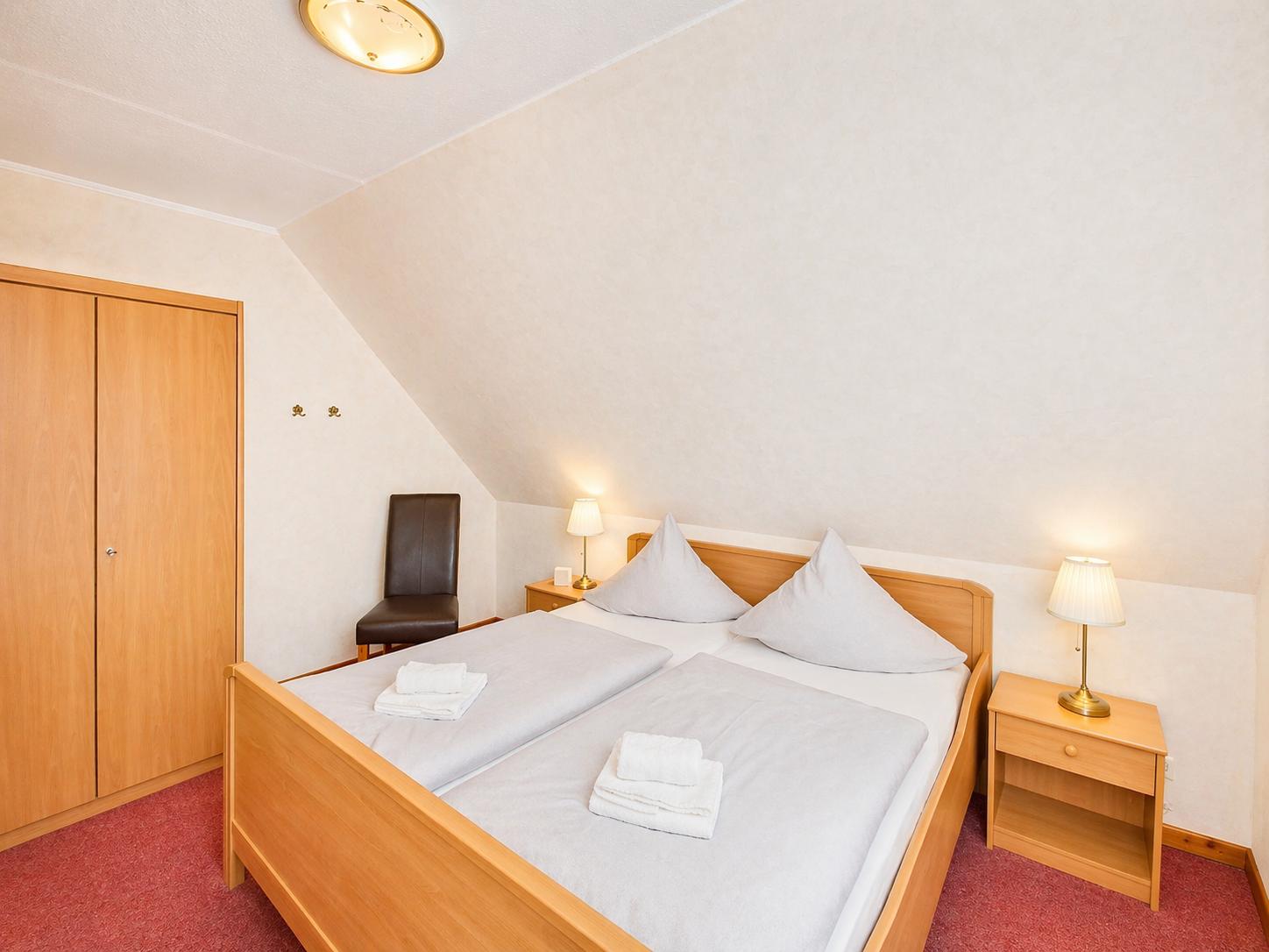 Schlafzimmer mit Doppelbett, Nachttischen und Kleiderschrank unter schrägem Dach.