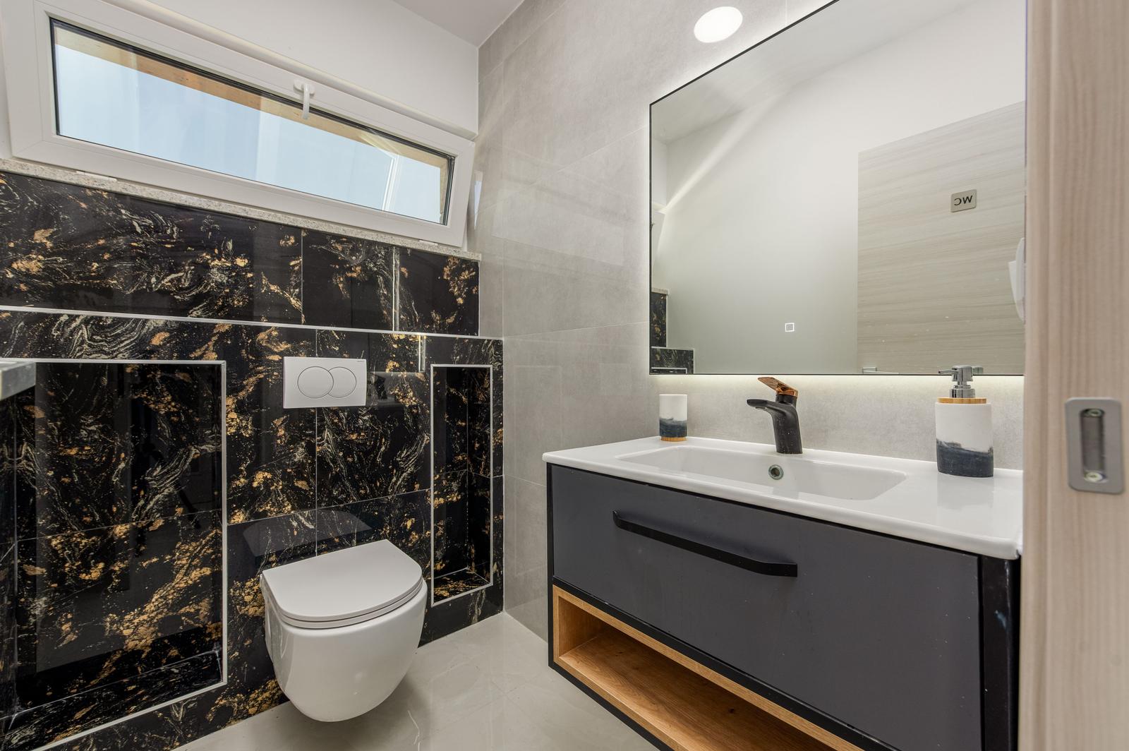 Badezimmer mit schwarzer Marmorwand, Waschtisch und Toilette.