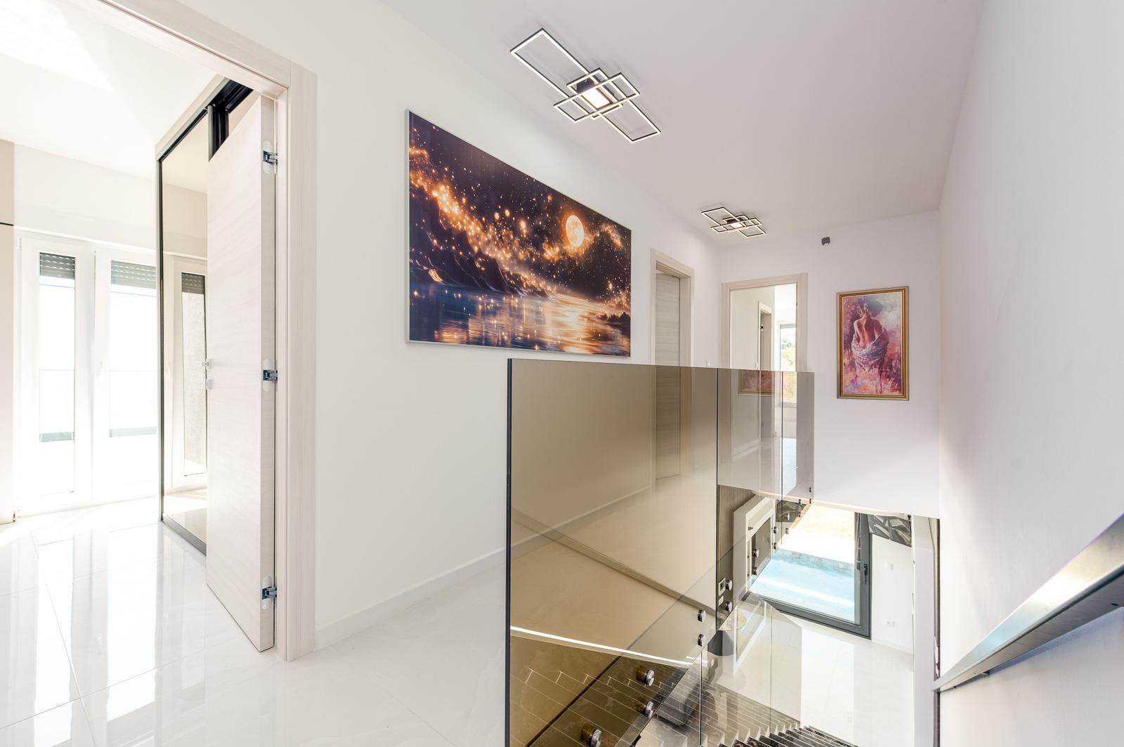 Haus mit Glasbrüstung, Wandbildern und weißen Wänden. Tür führt zu Terrasse.