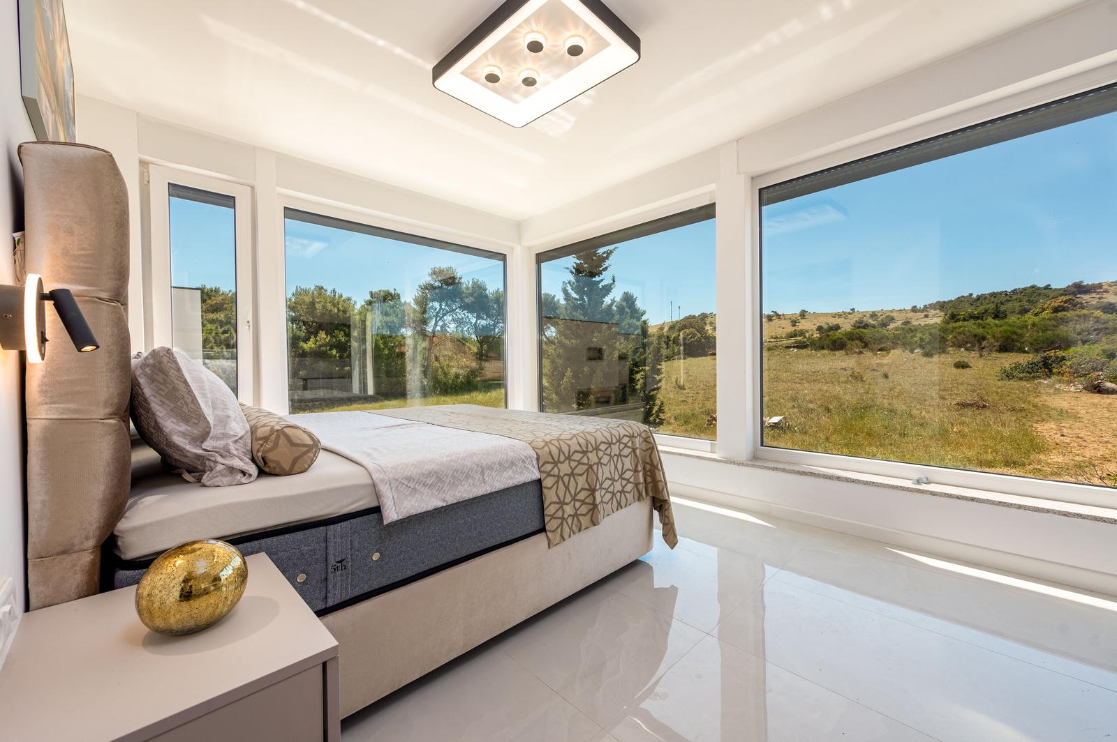 Schlafzimmer mit großem Bett und Fenstern zur Landschaft.
