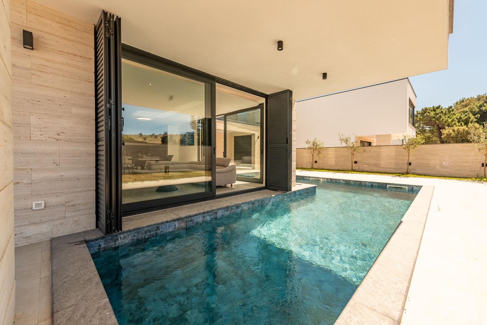 Pool mit Blick auf Wohnbereich durch große Glastüren.