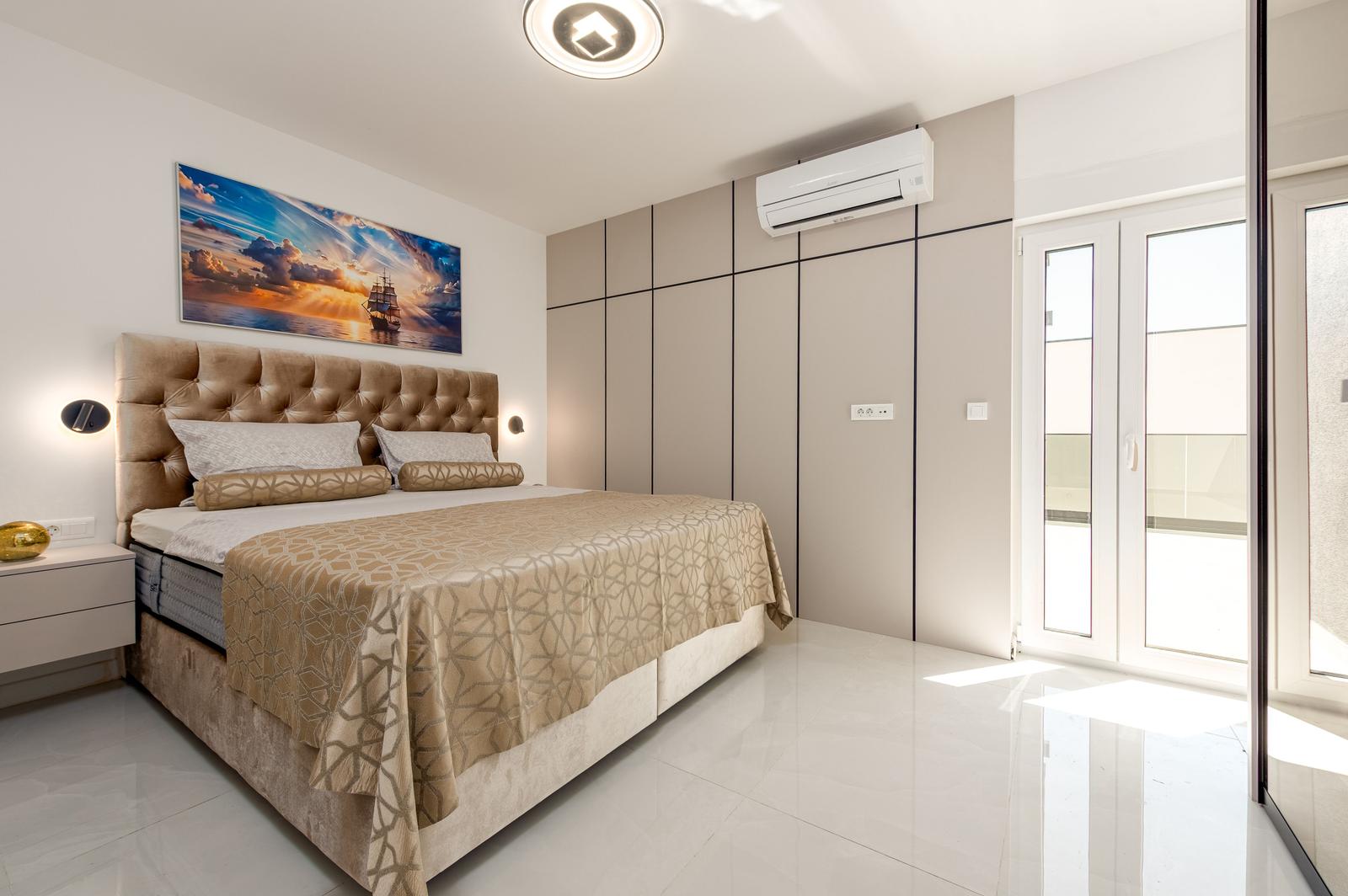Schlafzimmer mit großem Bett, Wandbild und bodentiefen Schiebetüren zur Terrasse.