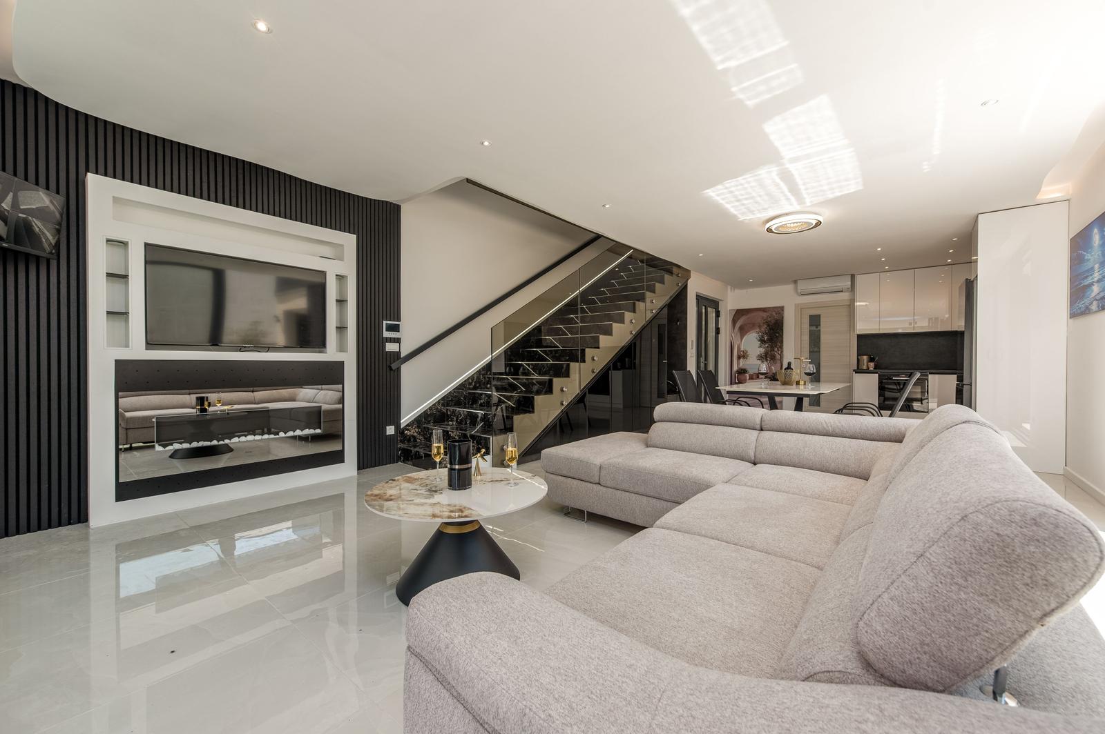 Großes Wohnzimmer mit Sofa, Glas-Treppe und Fernseher in moderner Einrichtung.