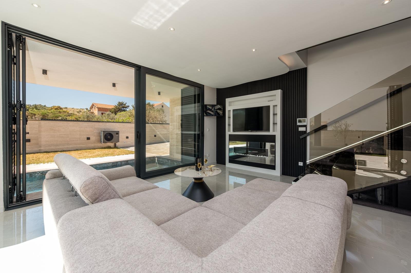 Großes Wohnzimmer mit Sofa, Fernseher und Blick auf Pool und Garten.