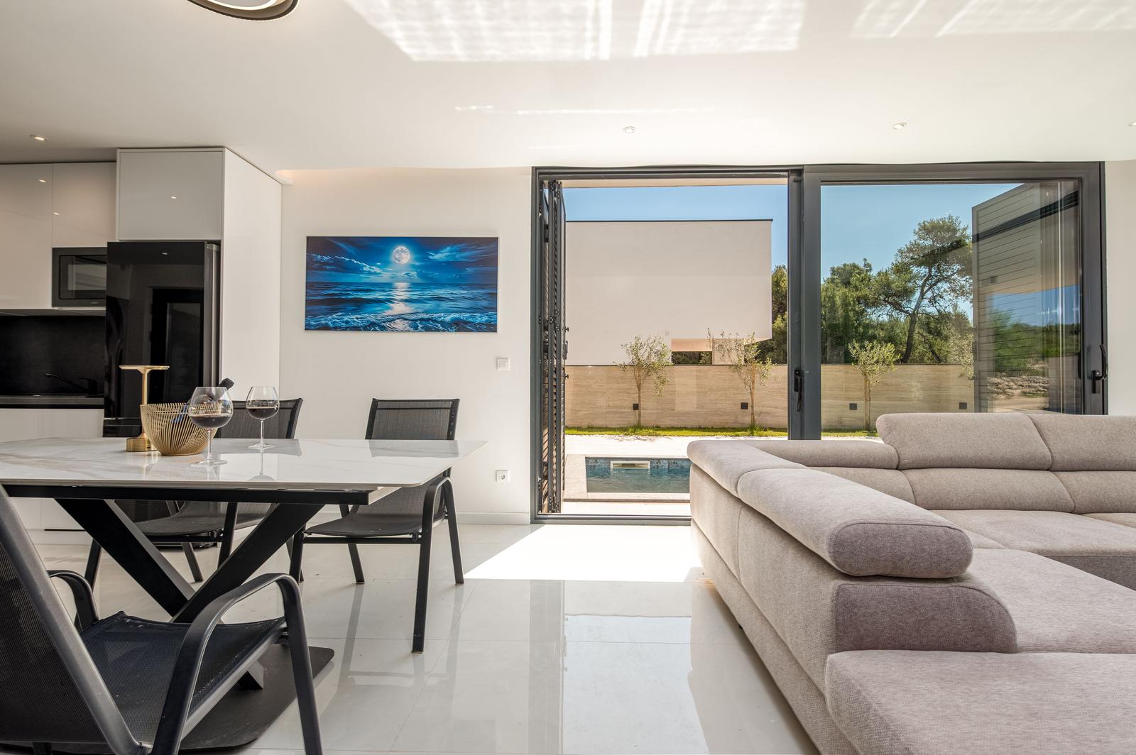 Wohn- und Essbereich mit Blick auf Pool und Garten. Moderne Einrichtung und Glaswände.