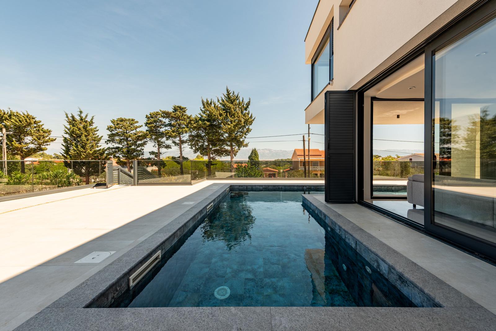 Moderne Villa mit Pool und Glasfront. Blick auf Bäume und Ferienhaus.