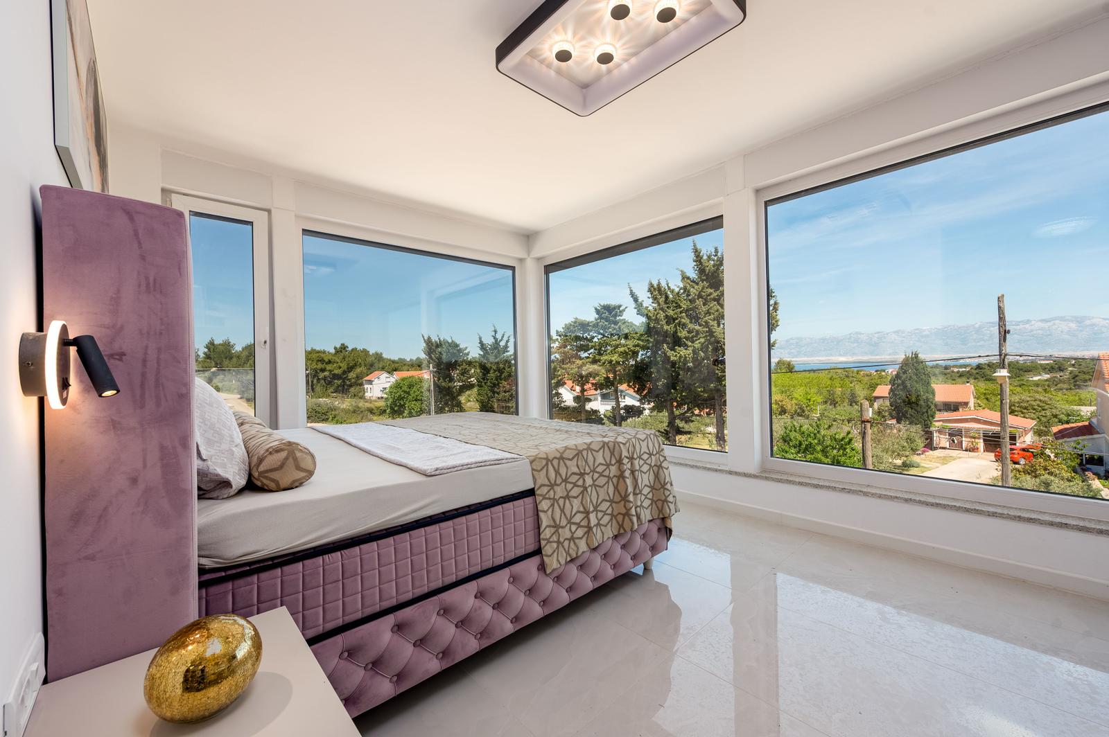 Schlafzimmer mit großem Fenster und Blick auf Landschaft.