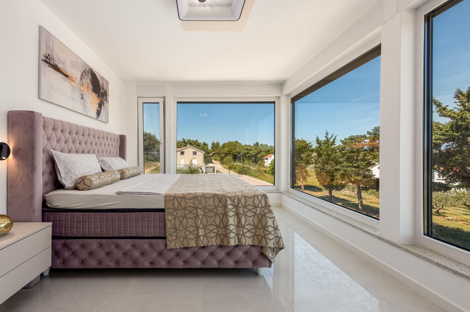 Schlafzimmer mit großem Bett und Blick auf Außenbereich durch Fenster