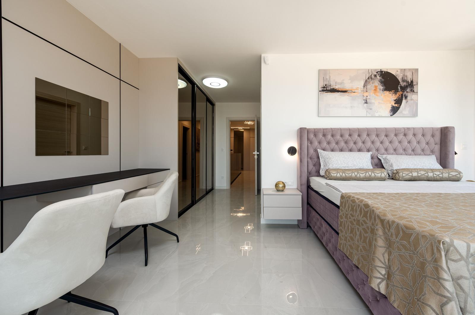 Schlafzimmer mit Bett, Schreibtisch und Spiegelschrank. Fliesenboden und Wandbild.