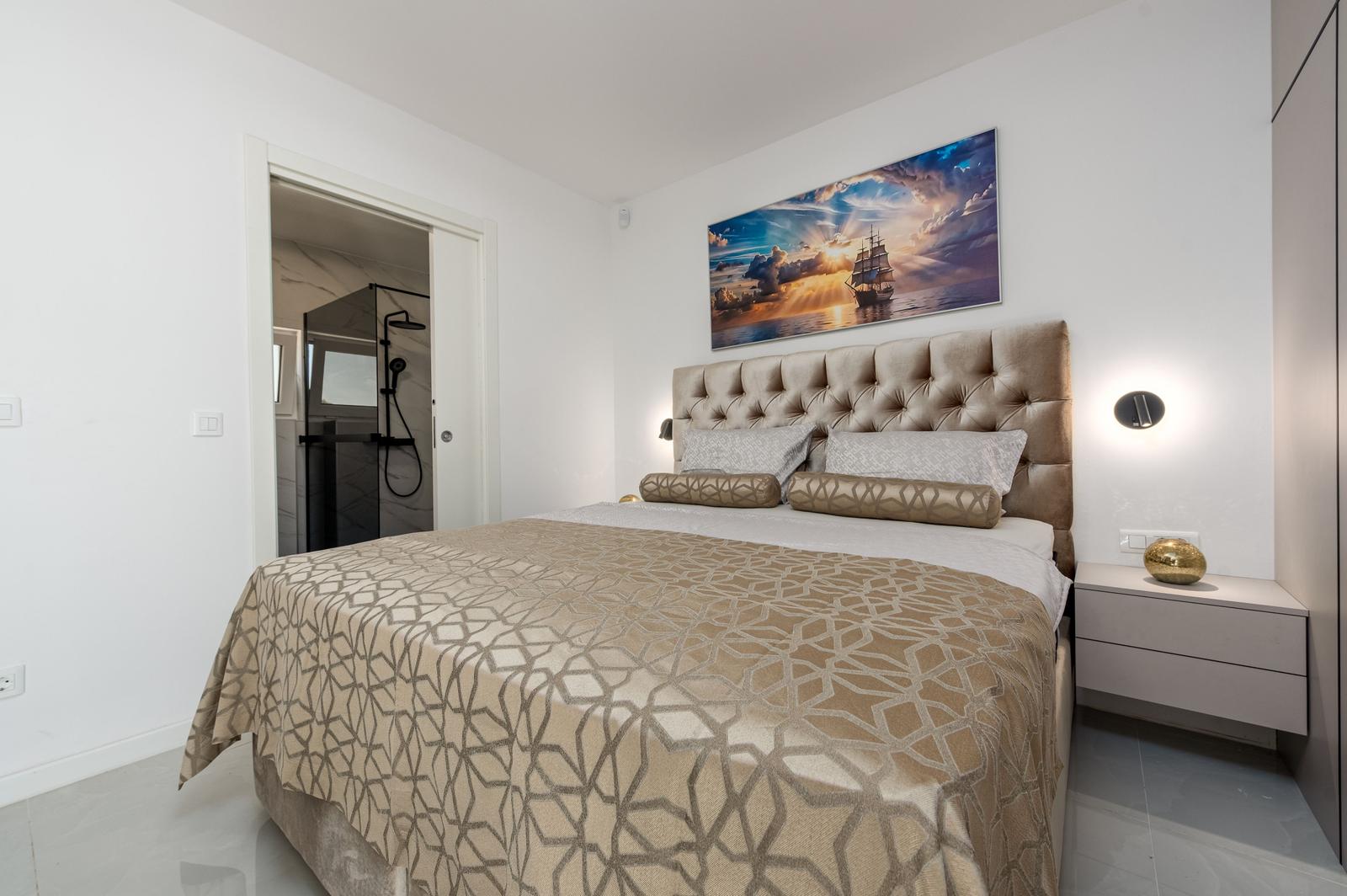 Schlafzimmer mit großem Bett, Wandbild und Anschluss zur Dusche.