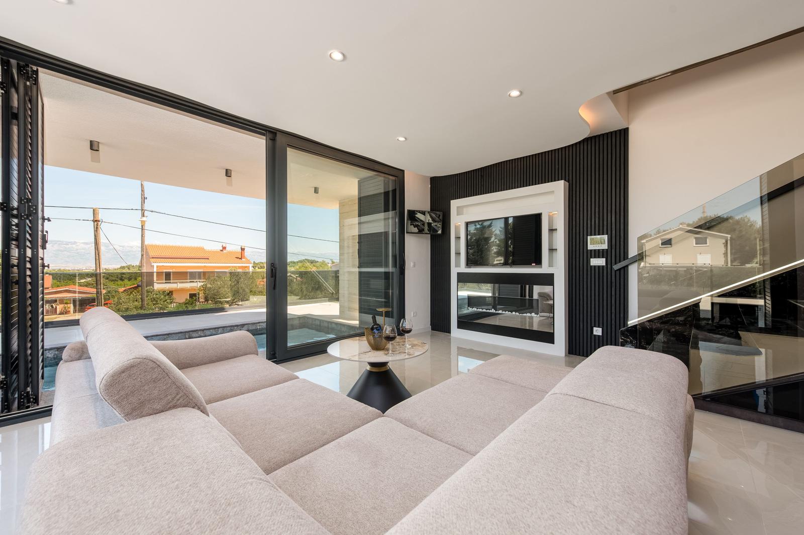 Großes Wohnzimmer mit Sofa, TV und Poolblick durch Glastüren.