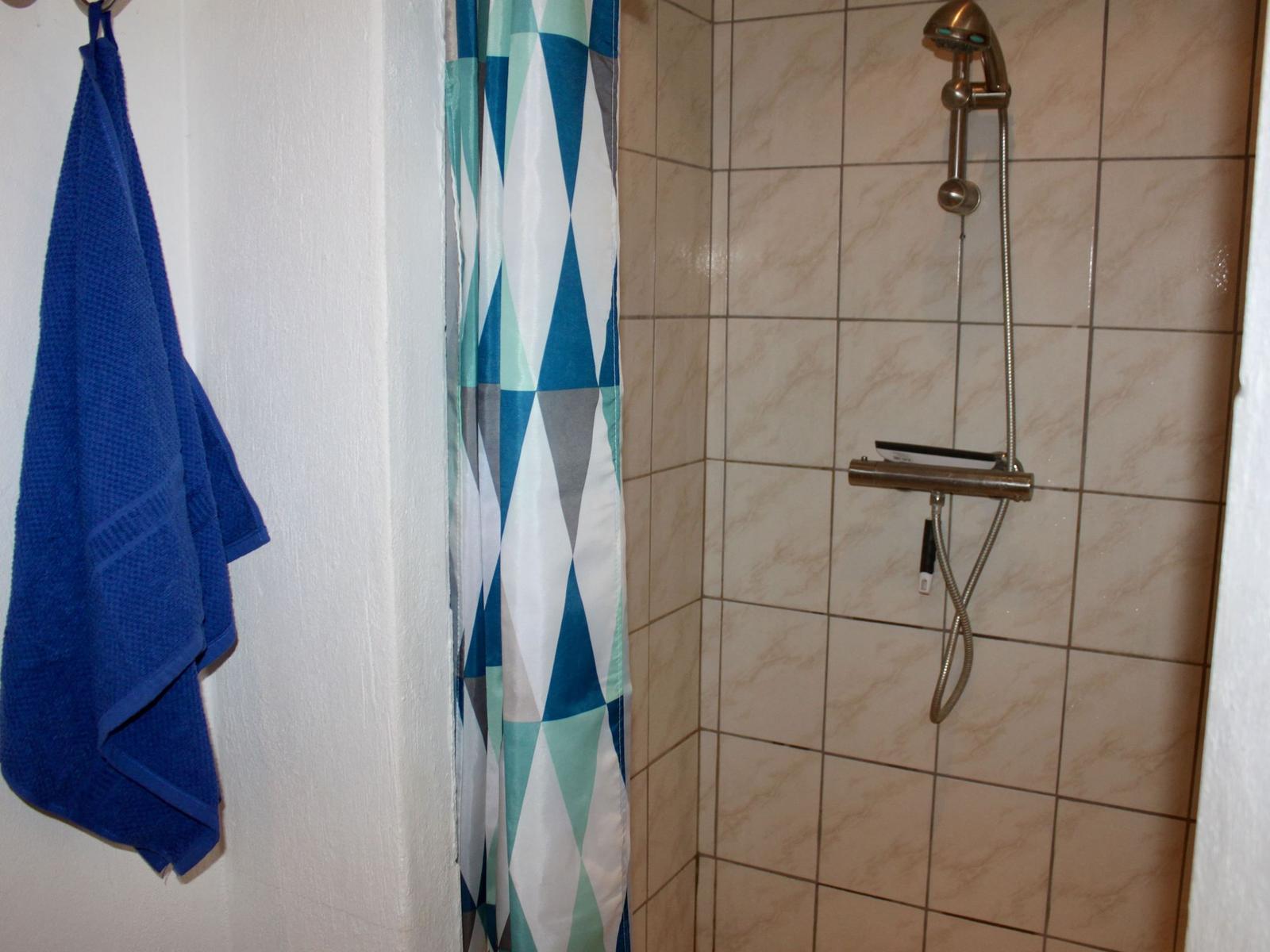 Dusche mit Duschvorhang und blauem Handtuch an der Wand.