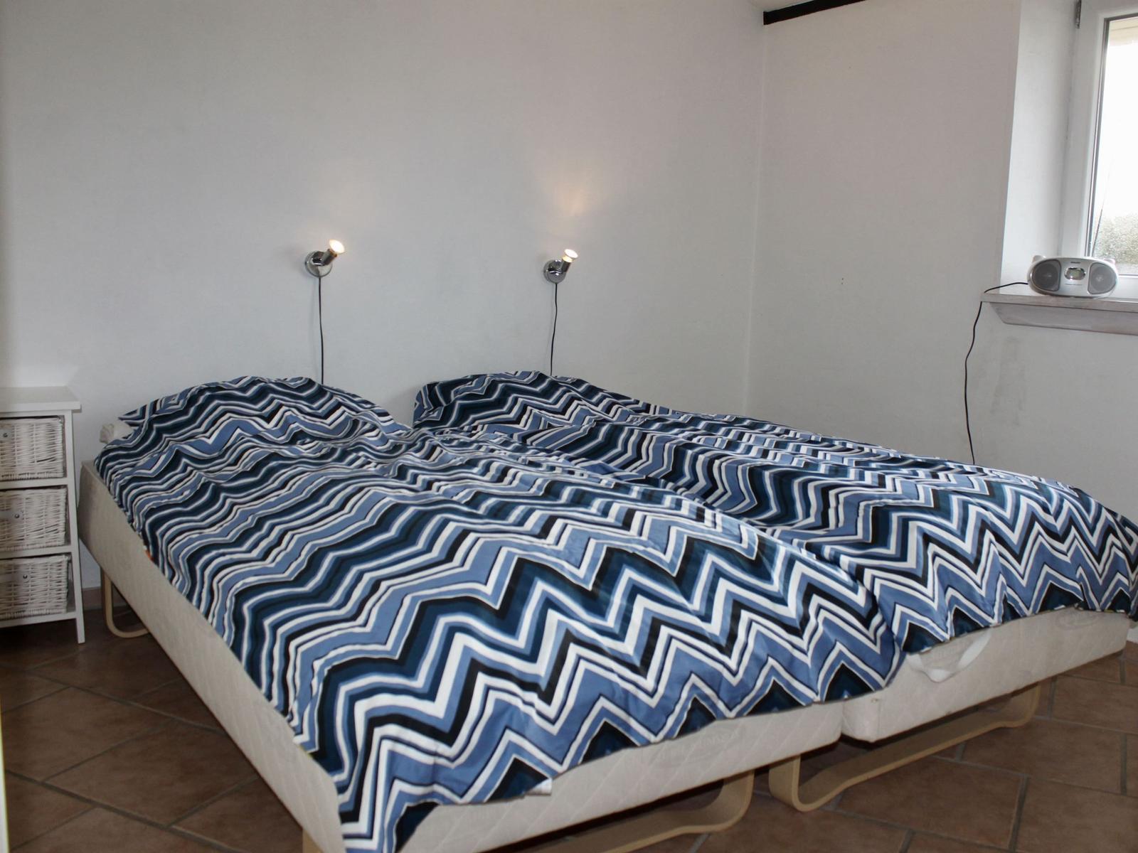 Schlafzimmer mit Doppelbett, blau-weißem Muster, Wandlampen und Fenster mit Radio.