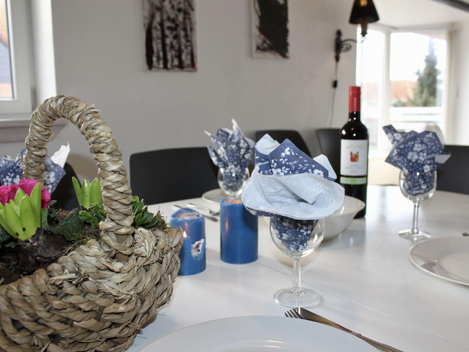 Gedeckter Tisch mit Blumenvase, Kerzen und Weinflasche.