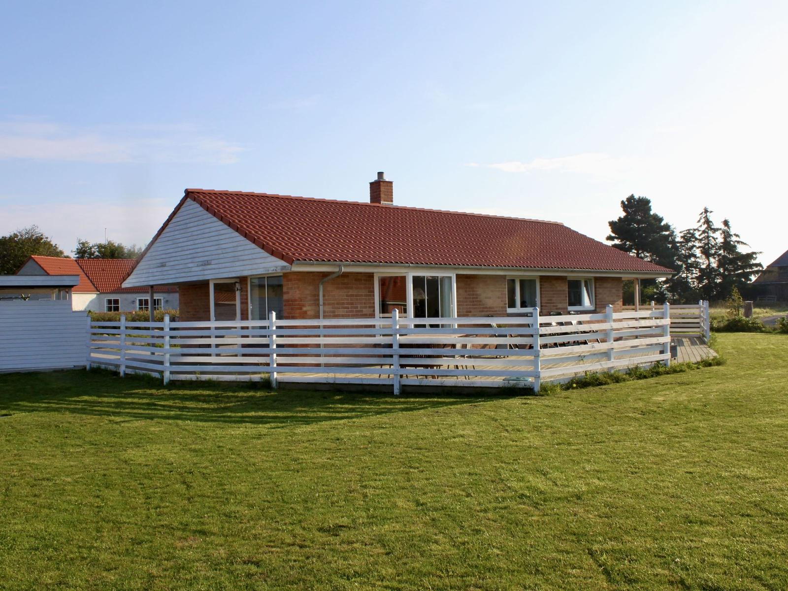 Ein Haus mit rotem Dach und weißem Zaun auf grünem Grund.