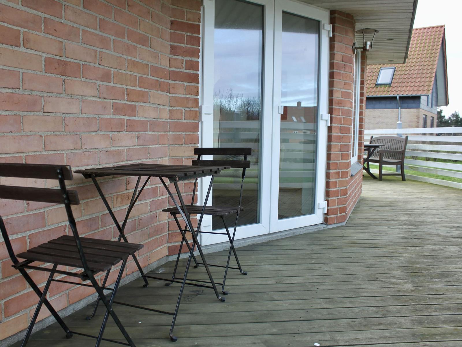 Terrasse mit Holzdecke, Tisch und Stühlen neben einer Glastür.